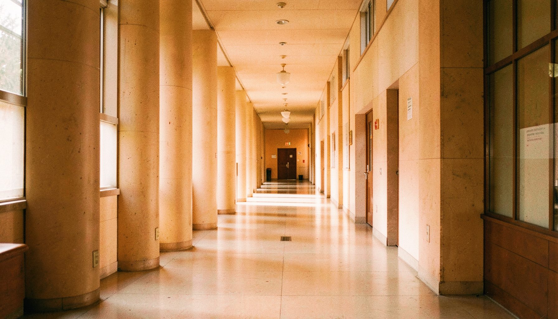 Pasillo de un edificio universitario con columnas y luz natural, tonos neutros y cálidos